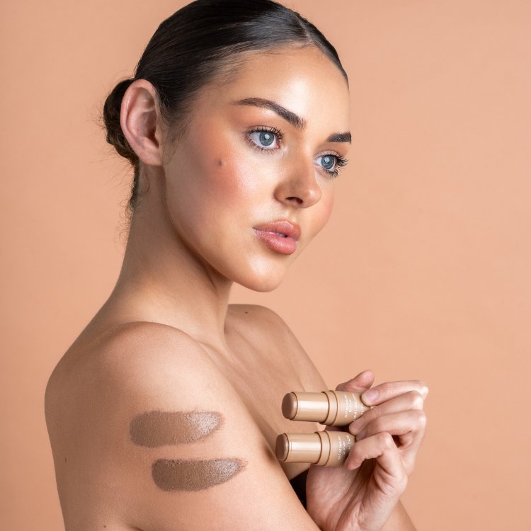 Woman holding makeup products against a beige background
