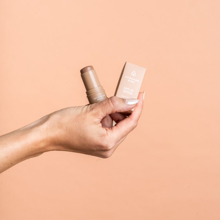 Hand holding a cosmetic bottle and its packaging against a beige background