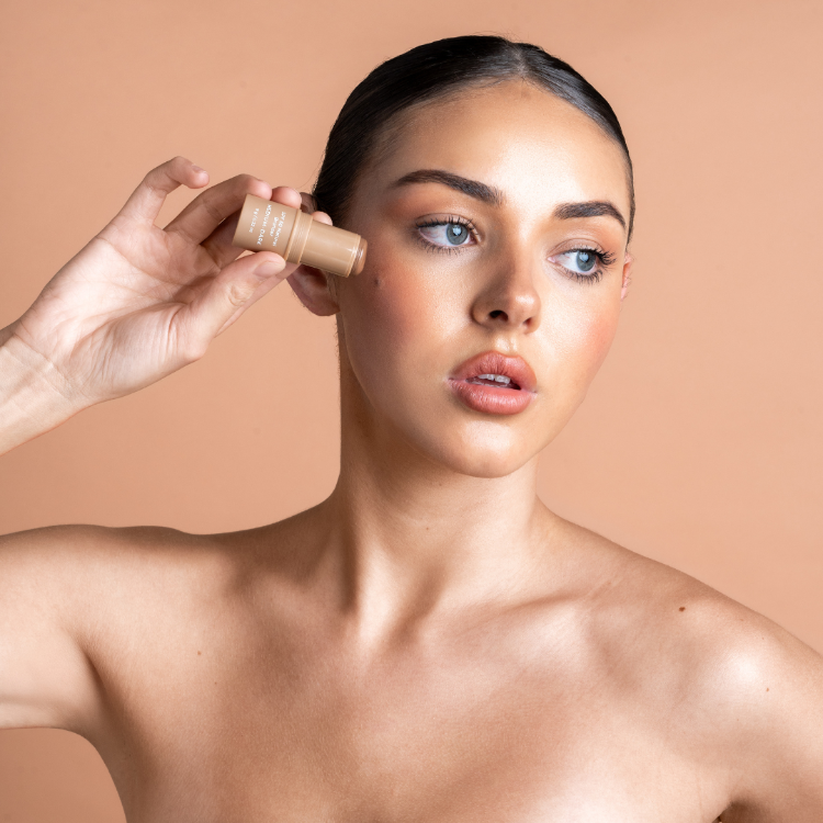 Woman applying makeup with a compact powder on a beige background