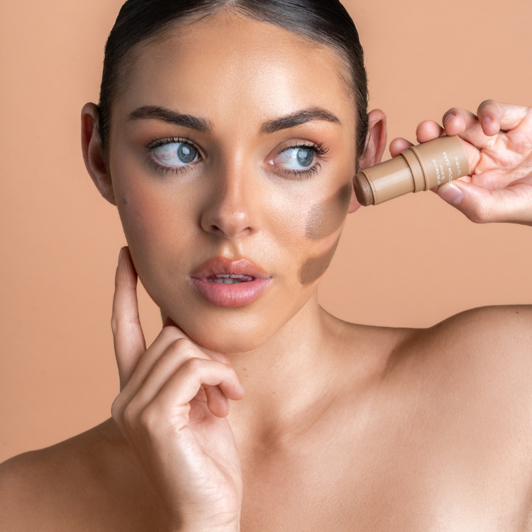 Woman applying foundation to her face with a brush on a beige background
