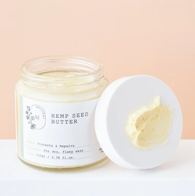 Jar of hemp seed butter with a spreadable portion on a white surface and pink background
