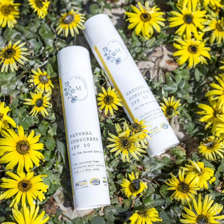 Two tubes of natural sunscreen surrounded by yellow flowers