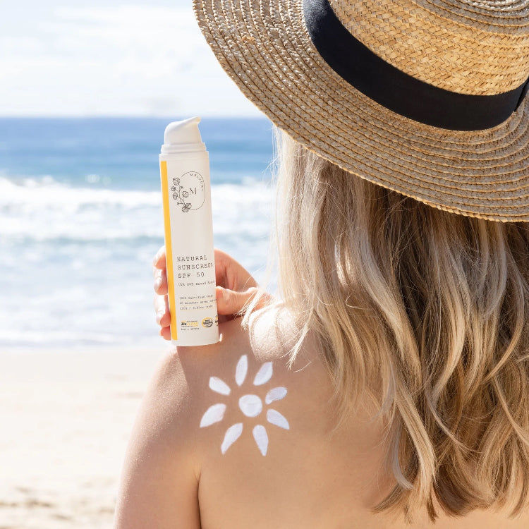 Person on a beach holding a bottle of sunscreen with a sunflower graphic on their shoulder.