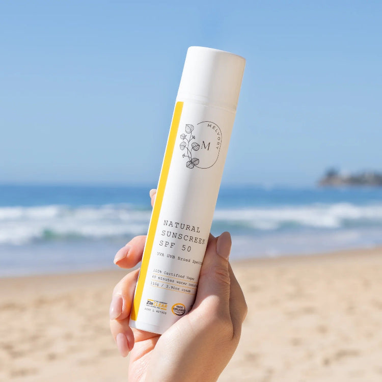 Hand holding a bottle of natural sunscreen with a beach background