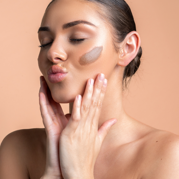 Woman applying makeup with brown concealer on a beige background