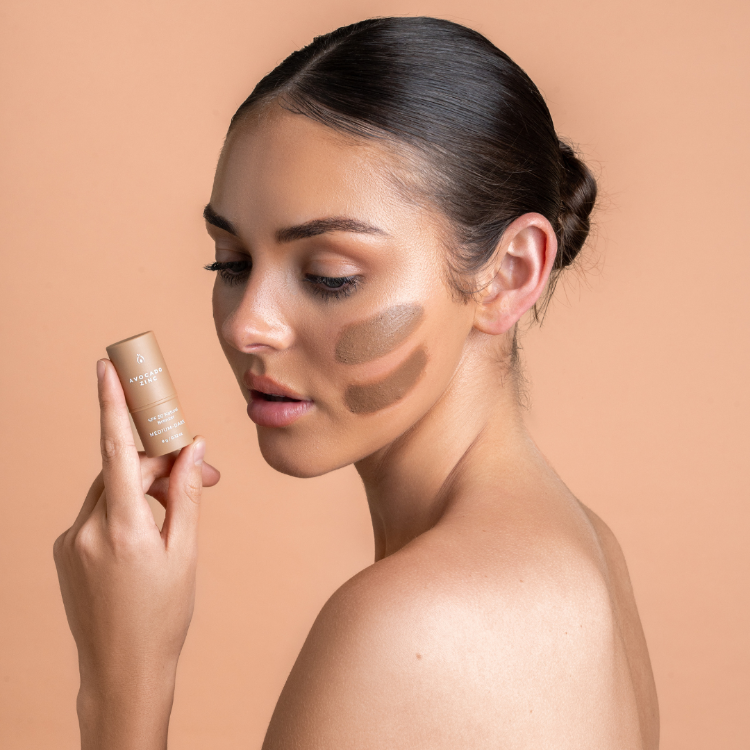 Woman applying makeup with a stick on a beige background